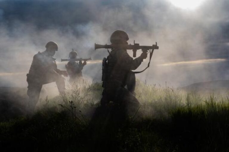 Soldiers in foggy field carrying heavy weapons